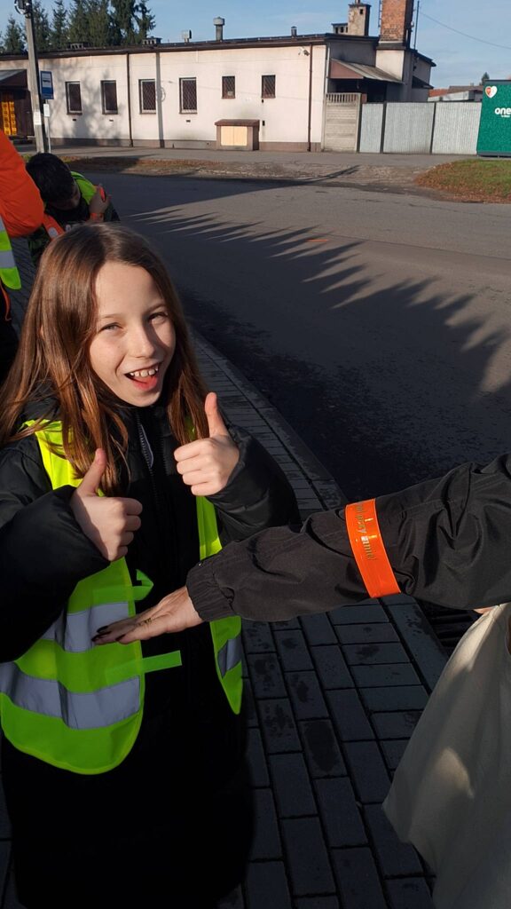 Odblaskowa Szkoła 2025- akcja rozdawania odblasków. Na zdjęciu uczennica zakłada kobiecie odblask na rękę. Uczennica uśmiecha się. 