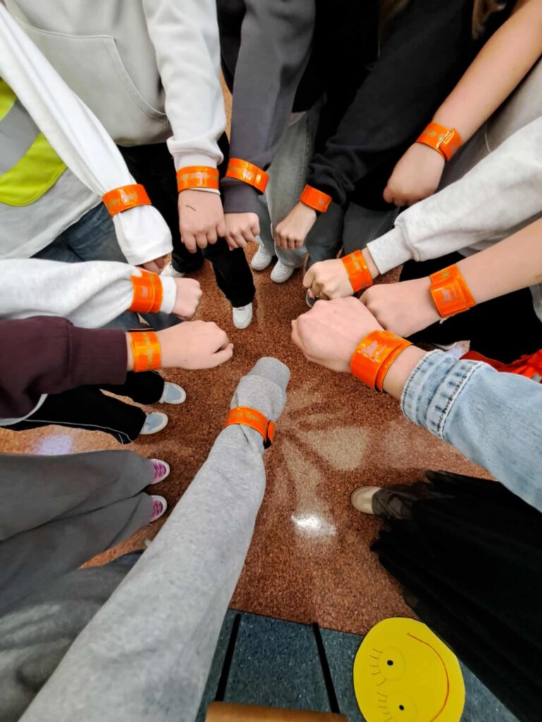 Odblaskowa Szkoła 2025- akcja rozdawania odblasków. Na zdjęciu wyciągnięte ręce uczniów z założonymi odblaskami. 