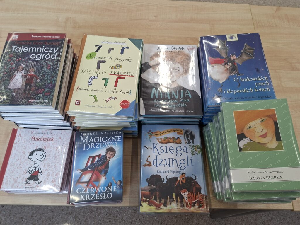 Przedstawia obłożone w przeźroczysta folię lektury szkolne. Kolorowe ilustracje na okładkach przedstawiają: skarpetki, chłopca siedzącego na czerwonym krześle, zwierzęta żyjące w dżungli, oraz dziewczynkę i chłopca w ogrodzie.