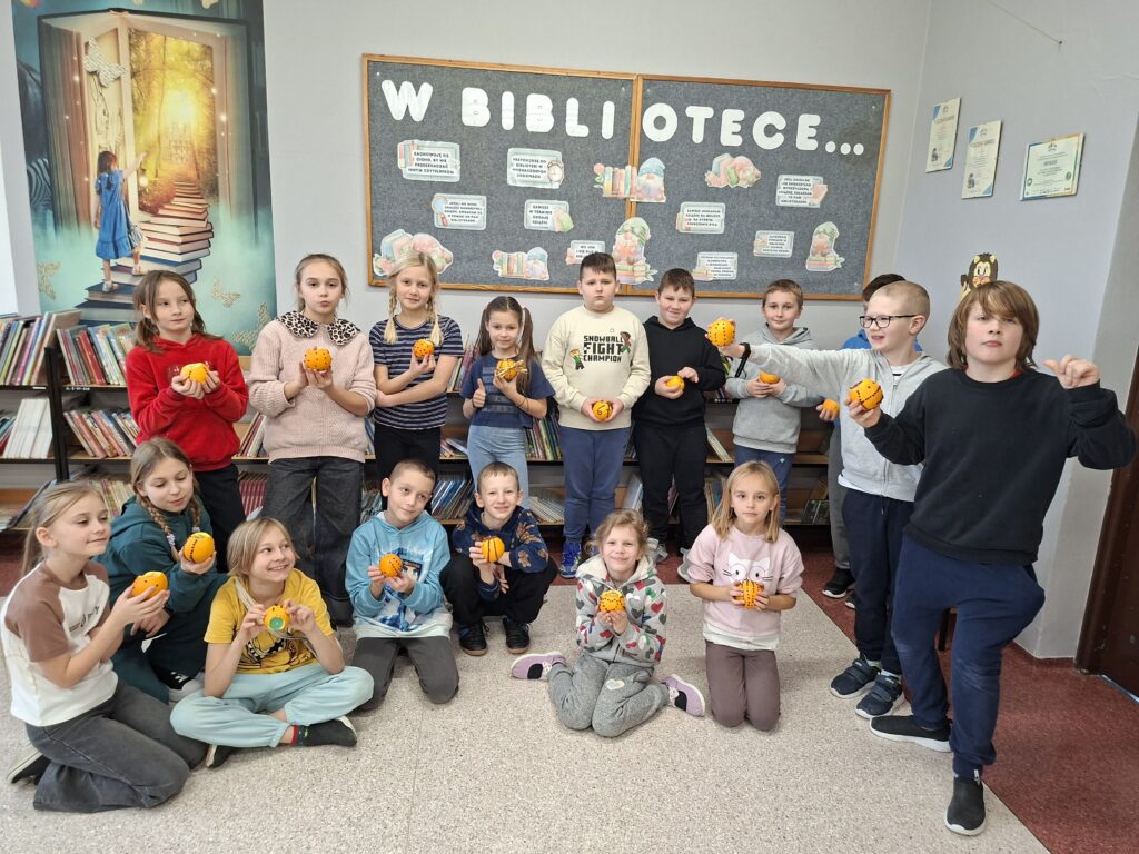 Warsztaty świąteczne w szkolnej bibliotece. Na zdjęciu uczniowie pokazują swoją pomarańczę ozdobioną suszonymi goździkami. 
