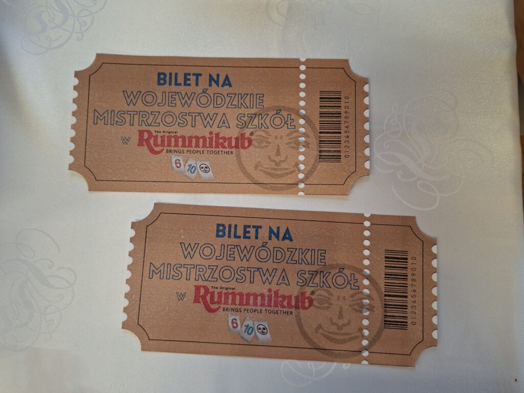 Przedstawia złote bilety na Mistrzostwa Wojewódzkie Szkół Rummikub. Na biletach są tabliczki z numerami 6, 10 i joker.