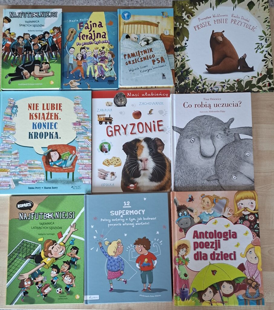 Przedstawia książki ułożone na stole obok siebie. Kolorowe Ilustracje okładek przedstawiają: dziewczynkę siedzącą na fotelu wśród książek, chomika, niedźwiadka oraz grupę chłopców na boisku piłki nożnej.