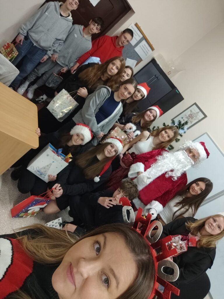 Mikołajki 2025. Na zdjęciu uczniowie klasy siódmej pozują do zdjęcia z Mikołajem. Uczniowie trzymają w ręce paczkę. 