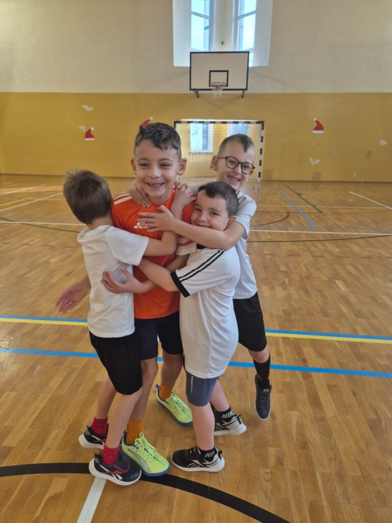 Turniej mikołajkowy. Na zdjęciu czterech uczniów są szczęśliwi po strzelonej bramce. obejmują się.