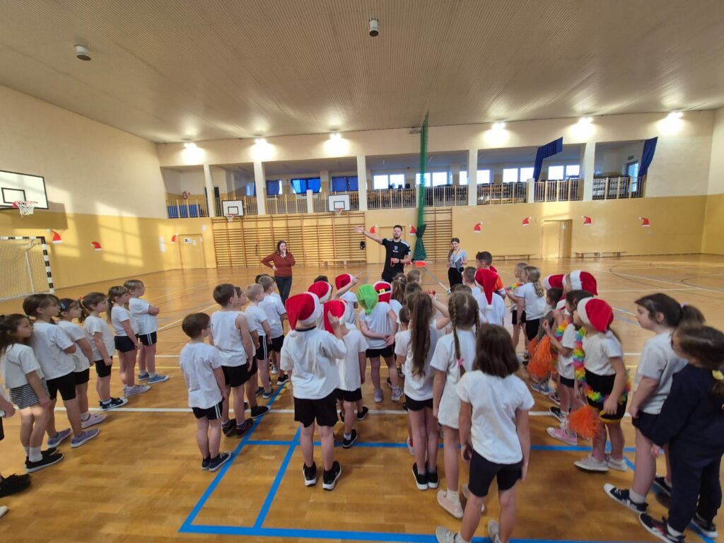 Turniej mikołajkowy. Na zdjęciu uczniowie ustawieni są w szeregu. Przed nimi stoi nauczycielka wuefistka i gość specjalny piłkarz.