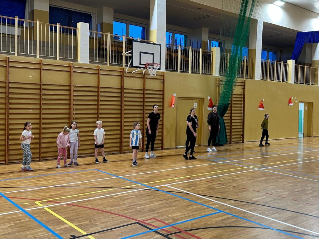 Wywiadówka z Kultury Fizycznej. Rodzice wraz ze swoimi dziećmi ustawieni są w jednym rzędzie, przygotowują się do wykonania ćwiczenia.