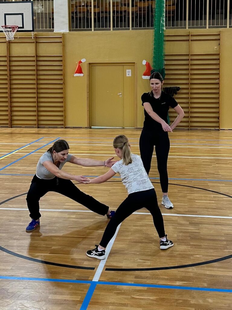 Wywiadówka z Kultury Fizycznej. Na zdjęciu dwie kobiety i uczennica. Nauczycielka wychowania fizycznego pokazuje ćwiczeni do wykonania.