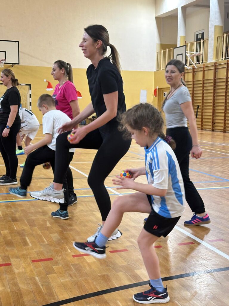 Wywiadówka z Kultury Fizycznej. Na zdjęciu mamy wraz dziećmi wykonują ćwiczeni: przekładania piłeczki po nogami.