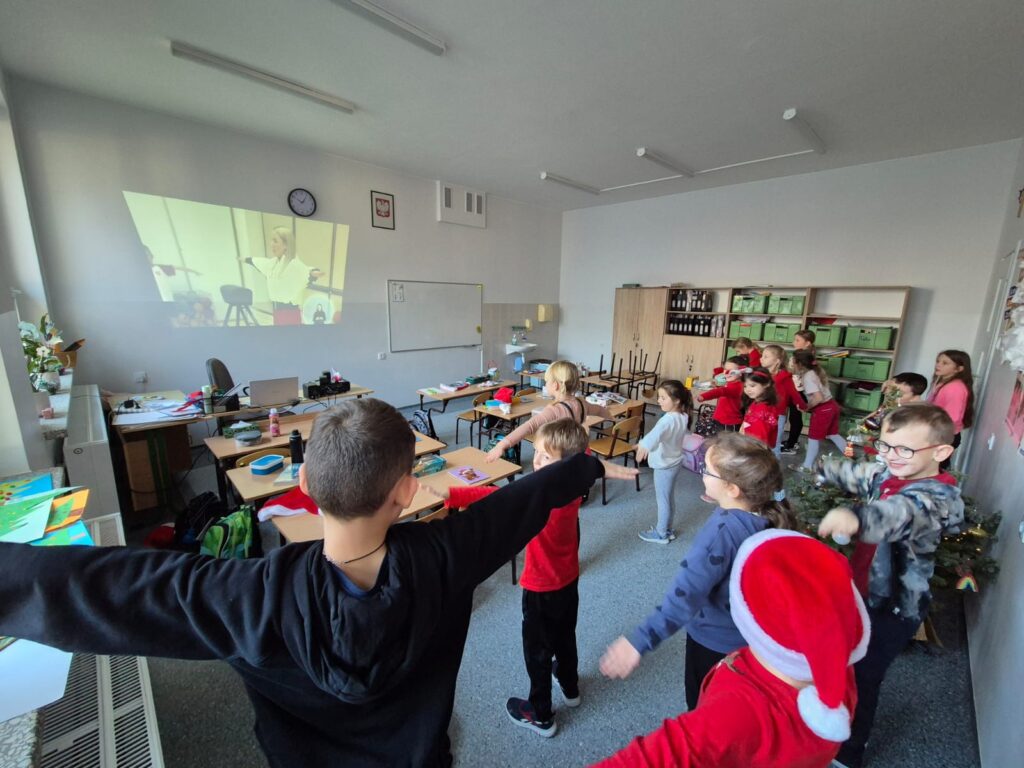 Integracyjny WF online - Tajemnica Świątecznej Fabryki. Na zdjęciu uczniowie wykonują ćwiczenia rękami według tego, co widzą na ekranie.