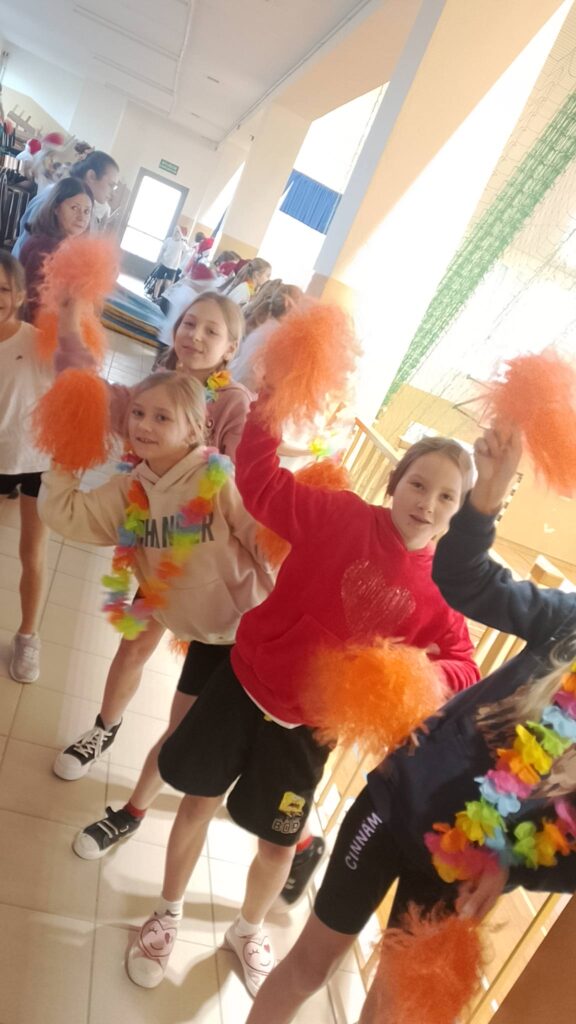 Turniej mikołajkowy. Uczennice jako
Cheerleaderki z pomarańczowymi pomponami kibicuje chłopcom podczas meczu.