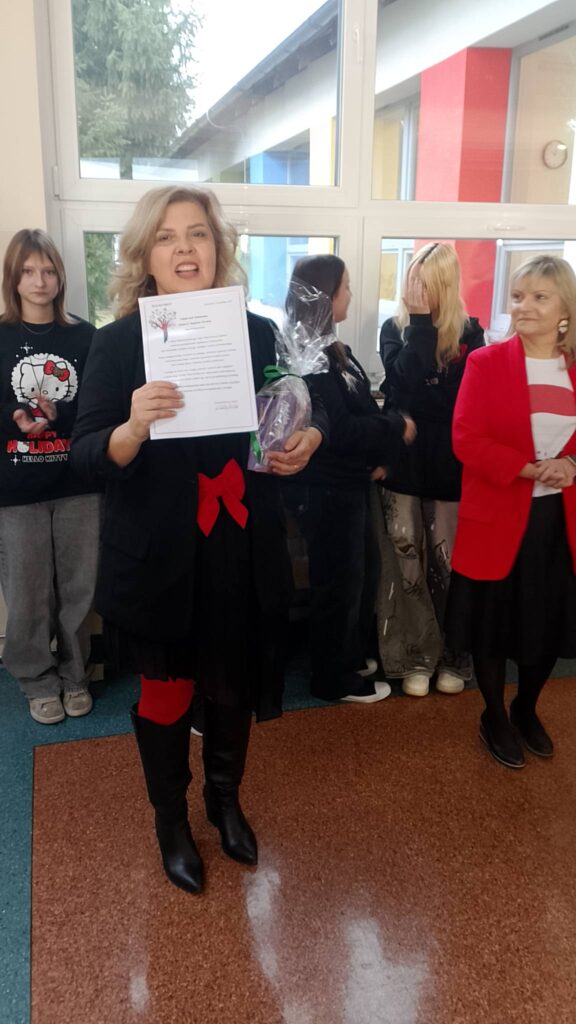 Mikołajki 2025. Na zdjęciu opiekunka szkolnego wolontariatu trzyma w ręce podziękowanie, za nią stoją inni uczniowie. 