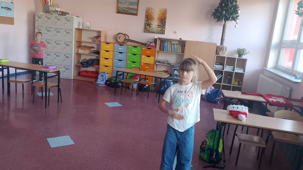 Integracyjny WF online - Tajemnica Świątecznej Fabryki. Na zdjęciu uczniowie wykonują ćwiczenia rękami według tego, co widzą na ekranie.