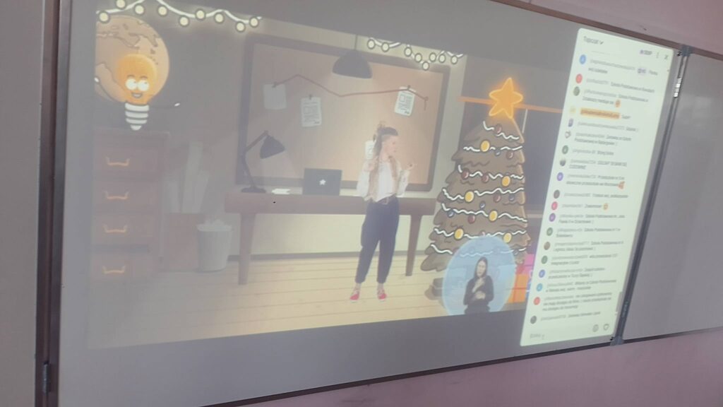 Integracyjny WF online - Tajemnica Świątecznej Fabryki. Na zdjęciu pani pokazuje ćwiczenia, po prawej stronie jest choinka.