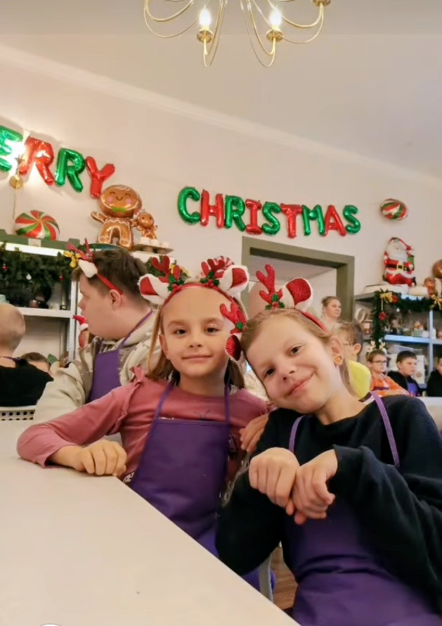 Świąteczne warsztaty ceramiczne w Chichach. Na zdjęciu uczennice pozują do zdjęcia, uśmiechają się, mają na głowie opaskę czerwoną z rogami renifera, w tle napis Merry Christmas.
