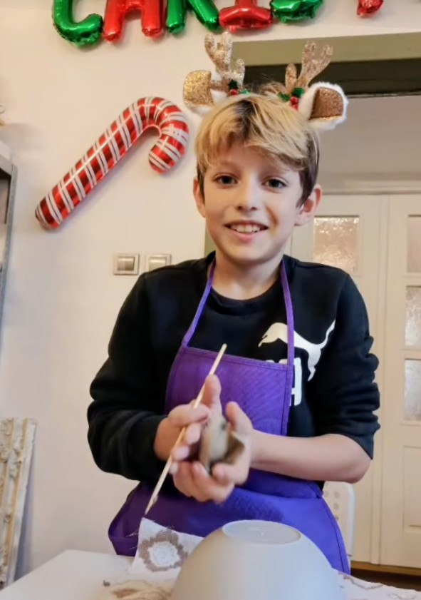 Świąteczne warsztaty ceramiczne w Chichach. Na zdjęciu uczeń uśmiecha się, na głowie ma opaskę z rogami renifera, w ręce trzyma kulkę gliny.