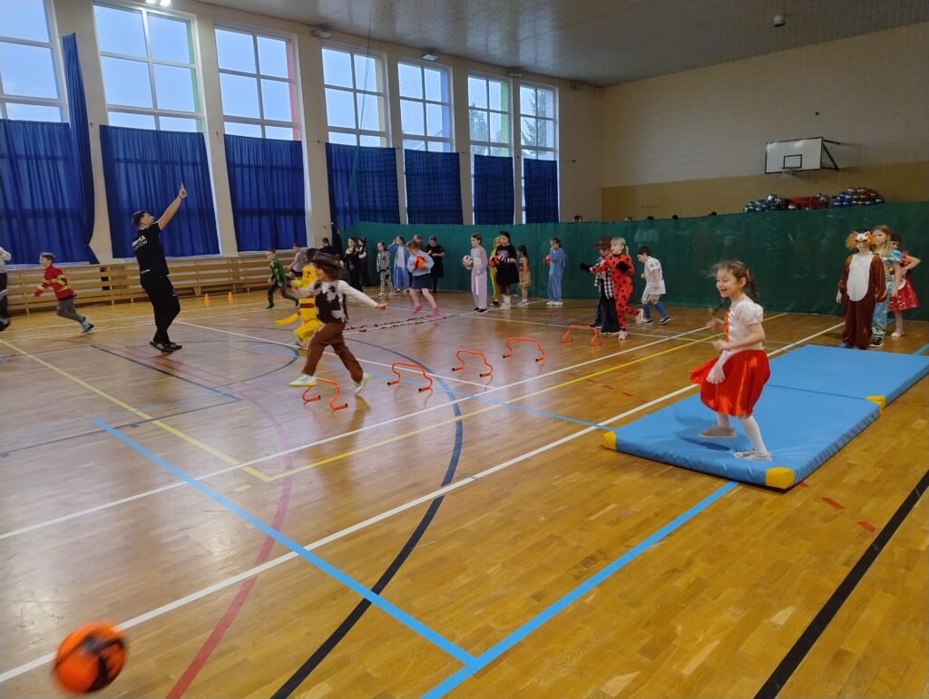 Uczniowie w przebraniach karnawałowych stoją ustawieni w kilku grupach przy stacjach z ćwiczeniami.