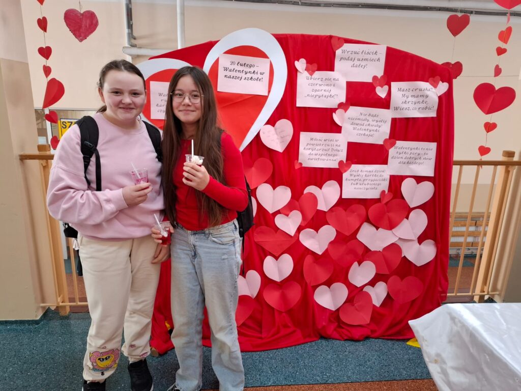 Na zdjęciu uczennice naszej szkoły zaangażowane w szkolną akcję - ,,Walentynki". Uczennice stojana tle czerwonej deokracji z serduszkami.
