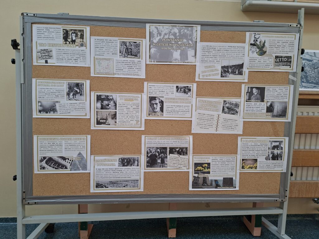 Przedstawia kartki przywieszone do korkowej tablicy z informacjami dot. powstania w getcie warszawskim. Informacje są w kolorystyce beżowej. Korkowa tablica ma czarne kółka.