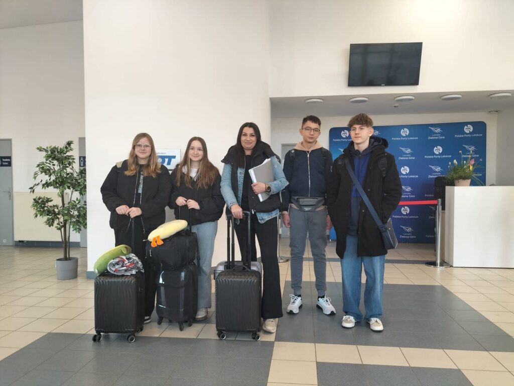 Nasi uczniwoie lecą do Chile. Na zdjęciu dwie uczennice, opiekunka i dwóch uczniów stoją w holu lotniska z walizkami.