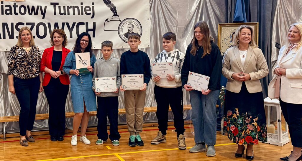 Zdjęcie przedstawia uczniów naszej szkoły trzymających dyplomy. Obok nich opiekun i organizatorzy turnieju. W tle zdjęcia baner z napisem "Międzypowiatowy Turniej Gier Planszowych" z logo szkoły Henrykiem Sienkiewiczem oraz dekoracja: biały lampion i portret patrona szkoły - Henryka Sienkiewicza.