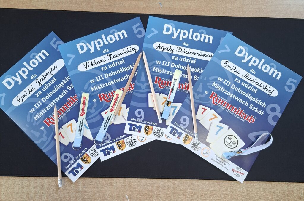 Zdjęcie przedstawia 4 dyplomy za udział w Dolnośląskich Mistrzostwach Szkół Rummikub. Na niebieskich dyplomach znajdują się upominki: beżowe ołówki i białe smycze.