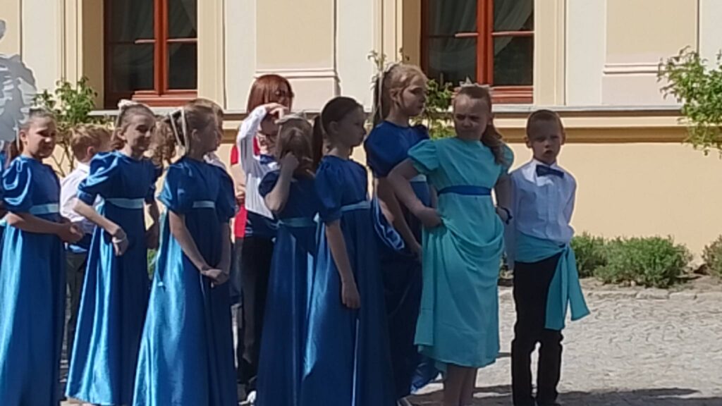 Obchody rocznicy uchwalenia Konstytucji 3 Maja. Uczennice obrane w długie szafirwoe sukienki i chłopcy w białe koszule i ciemne spodnie stoją przed pałacem czekając na występ- taniec polonez. 