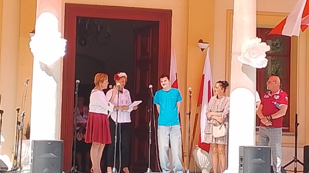 Obchody rocznicy uchwalenia Konstytucji 3 Maja. Na zdjęciu pani Dyrektor szkoły wita ucznia, dla którego jest prowadzona zbiórka pieniędzy, życzy mu powrotu do całkowitego zdrowia.  