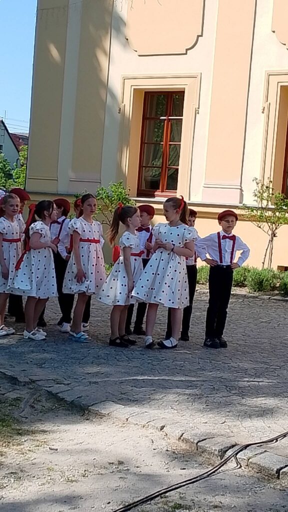 Obchody rocznicy uchwalenia Konstytucji 3 Maja. Na zdjęciu dziewczynki ubrane w białe sukienki z czerwonymi grochami i chłopcy ubrani w białe koszule, ciemne spodnie, czerwone szelki i czerwone kaszkiety czekają na wykonanie tańca polki. 