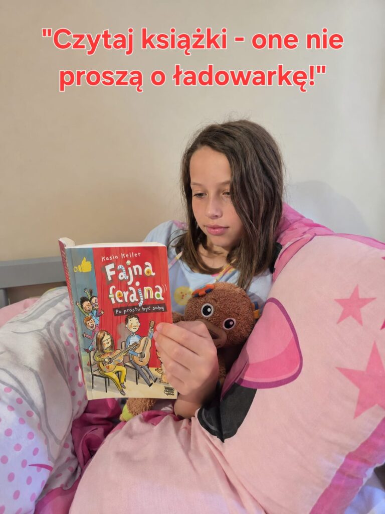 Na zdjęciu widać dziewczynkę siedzącą wygodnie w łóżku, otuloną różową pościelą i opartą o dużą poduszkę. Skupiona czyta książkę „Fajna ferajna. Po prostu być sobą” autorstwa Kasi Keller. W jednej ręce trzyma książkę, a drugą przytula pluszową zabawkę, co nadaje scenie ciepły i przytulny charakter.

Nad jej głową znajduje się napis: „Czytaj książki – one nie proszą o ładowarkę!”, który zachęca do czytania i podkreśla zalety tradycyjnych książek w świecie pełnym urządzeń elektronicznych.