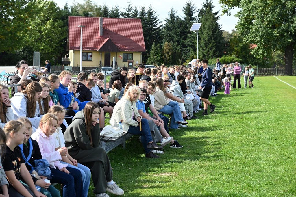 Na zdjęciu widzimy licznie zgromadzonych uczniów, którzy z zainteresowaniem obserwują przebieg „Porowej sztafety”. Uczestnicy siedzą wzdłuż szkolnego boiska, tworząc publiczność i wspierając swoich kolegów oraz koleżanki podczas sportowej rywalizacji.
Fotografia pokazuje, że akcja „Aktywność rodzi pozytywność” była wydarzeniem integrującym całą społeczność uczniowską.
