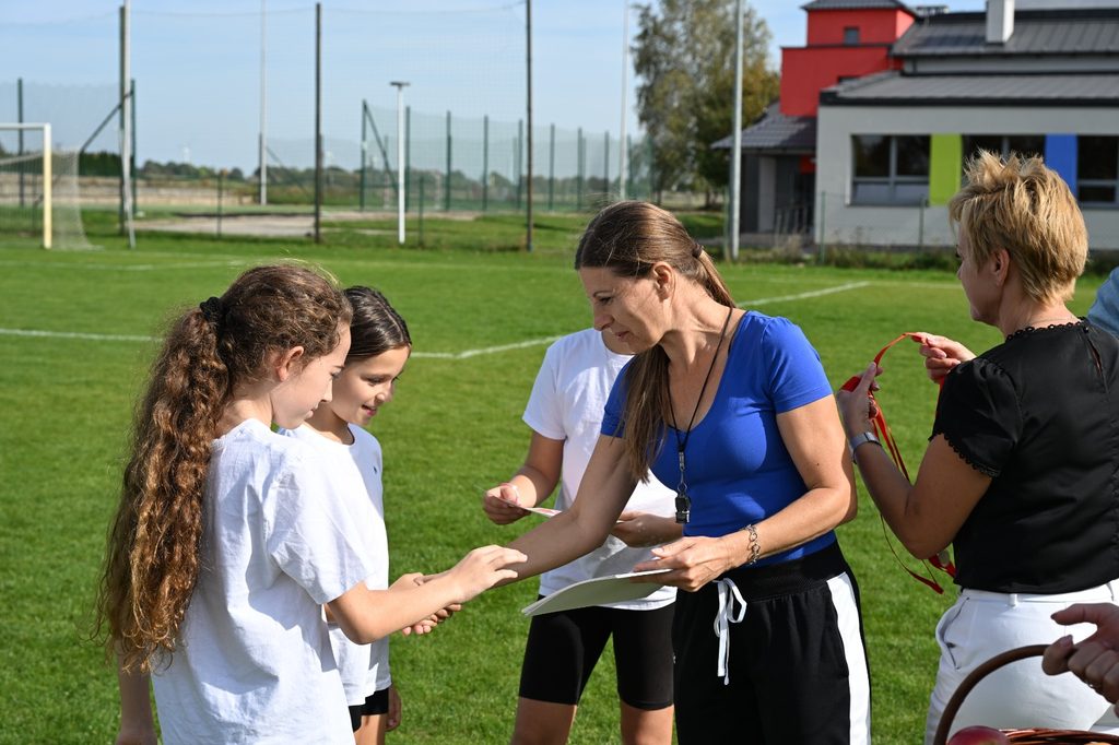 Na zdjęciu uchwycono moment wręczania nagród uczestnikom „Porowej sztafety”. Po zakończeniu sportowych zmagań uczniowie otrzymują pamiątkowe medale i dyplomy, będące nagrodą za zaangażowanie, wysiłek oraz udział w rywalizacji.
Fotografia pokazuje jeden z ważniejszych momentów akcji „Aktywność rodzi pozytywność” – docenienie każdego uczestnika i podkreślenie, że w sportowej zabawie liczą się nie tylko wyniki, ale również aktywność, współpraca, zaangażowanie i radość ze wspólnie spędzonego czasu.