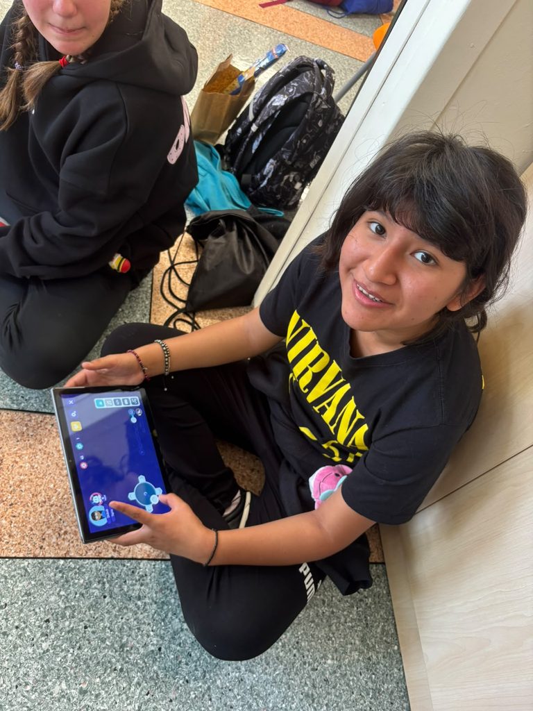Nauka programowania z robotami Photon – technologia bez granic!
Na zdjęciu widzimy uśmiechniętą uczestniczkę międzynarodowego spotkania z uczniami z Chile, która prezentuje tablet z aplikacją służącą do sterowania robotem edukacyjnym Photon. Dzięki intuicyjnemu interfejsowi uczniowie mogą samodzielnie programować ruchy robota, wyznaczać trasy i obserwować efekty swoich działań.