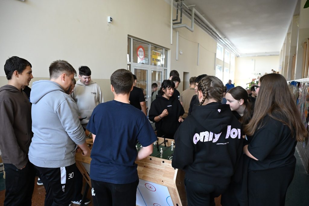 Na zdjęciu widzimy grupę młodzieży zgromadzoną wokół stołu do gry w piłkarzyki. Uczestnicy wspólnie biorą udział w rozgrywce, obserwują jej przebieg i rozmawiają ze sobą. Widać duże zainteresowanie wspólną aktywnością i zaangażowanie młodzieży.
Fotografia przedstawia integracyjne spotkanie w przyjaznej i swobodnej atmosferze. Wspólna gra sprzyja budowaniu relacji rówieśniczych, rozwijaniu umiejętności współpracy i komunikacji, a także uczy przestrzegania zasad oraz zdrowej rywalizacji. Jest to również okazja do aktywnego i wartościowego spędzania czasu w grupie.