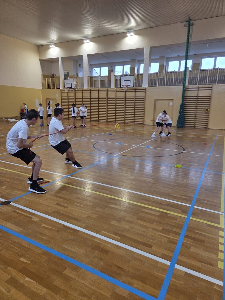 Zdjęcie przedstawia czterech uczniów przeciągających linę. Znajdują się na sali gimnastycznej i są ubrani w stroje sportowe.