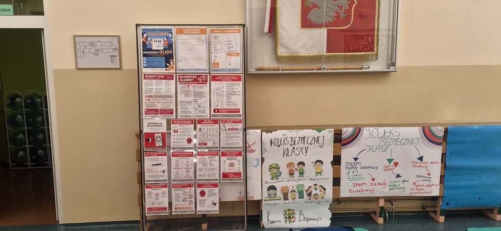 Na zdjęciu przedstawiono wystawę edukacyjną przygotowaną w ramach Krajowego Treningu Rodzinnego – Akademii Ochrony Ludności i Obrony Cywilnej (OLiOC).
Na szkolnym korytarzu zaprezentowano materiały informacyjne dotyczące bezpieczeństwa, zasad reagowania na alarmy, Alertów RCB, przygotowania rodzinnego planu bezpieczeństwa, ewakuacji oraz właściwego postępowania w sytuacjach kryzysowych.