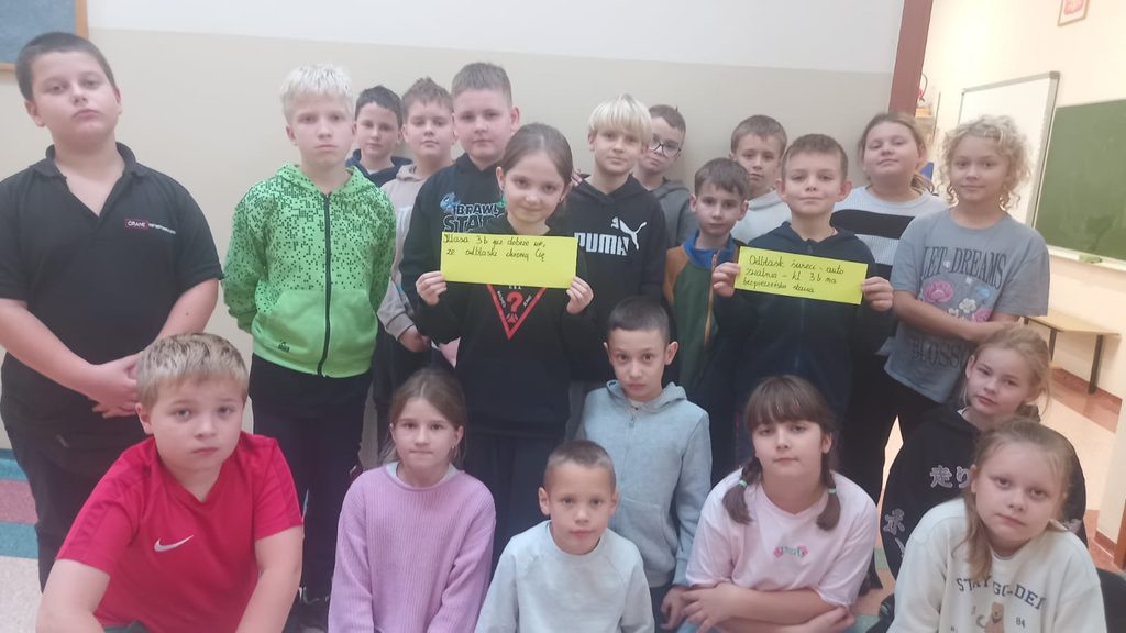 „Odblaskowa Szkoła” – uczniowie klas III promują bezpieczeństwo na drodze!
Na zdjęciu widoczna jest grupa uśmiechniętych uczniów, którzy prezentują własnoręcznie przygotowane hasła zachęcające do noszenia elementów odblaskowych. Dzieci trzymają jasnożółte kartki z rymowankami podkreślającymi znaczenie odblasków dla bezpieczeństwa pieszych.