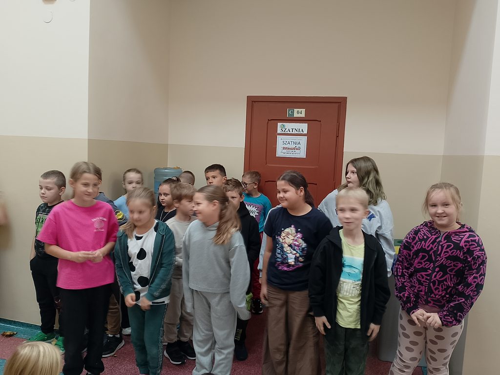 Na zdjęciu widzimy grupę uczniów zgromadzonych na szkolnym korytarzu podczas wspólnego wydarzenia. Dzieci stoją razem, uśmiechają się i z zainteresowaniem obserwują to, co dzieje się wokół nich.
Fotografia ukazuje radosną i swobodną atmosferę oraz integrację uczniów. Wspólne spotkanie jest okazją do budowania relacji, wzajemnej współpracy i poczucia przynależności do społeczności szkolnej.