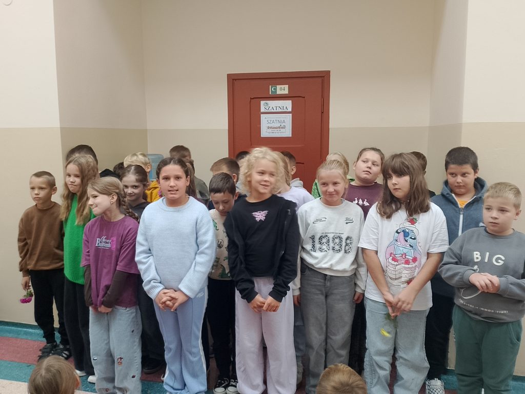 Na zdjęciu widzimy grupę uczniów zgromadzonych na szkolnym korytarzu podczas wspólnego wydarzenia. Dzieci stoją razem, uśmiechają się i z zainteresowaniem obserwują to, co dzieje się wokół nich.
Fotografia ukazuje radosną i swobodną atmosferę oraz integrację uczniów. Wspólne spotkanie jest okazją do budowania relacji, wzajemnej współpracy i poczucia przynależności do społeczności szkolnej.