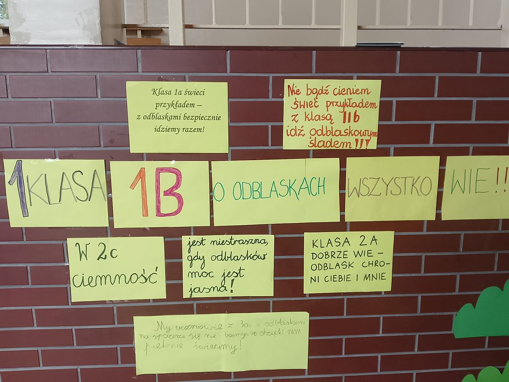 Na zdjęciu widoczna jest kolorowa wystawa haseł promujących noszenie elementów odblaskowych, przygotowana przez uczniów klas I–III w ramach ogólnopolskiej akcji „Odblaskowa Szkoła”.

Na szkolnym korytarzu, na ścianie z czerwonej cegły, umieszczono plakaty wykonane na jasnożółtych kartkach. Uczniowie wykazali się kreatywnością, tworząc rymowane hasła zachęcające do noszenia odblasków i dbania o bezpieczeństwo na drodze.